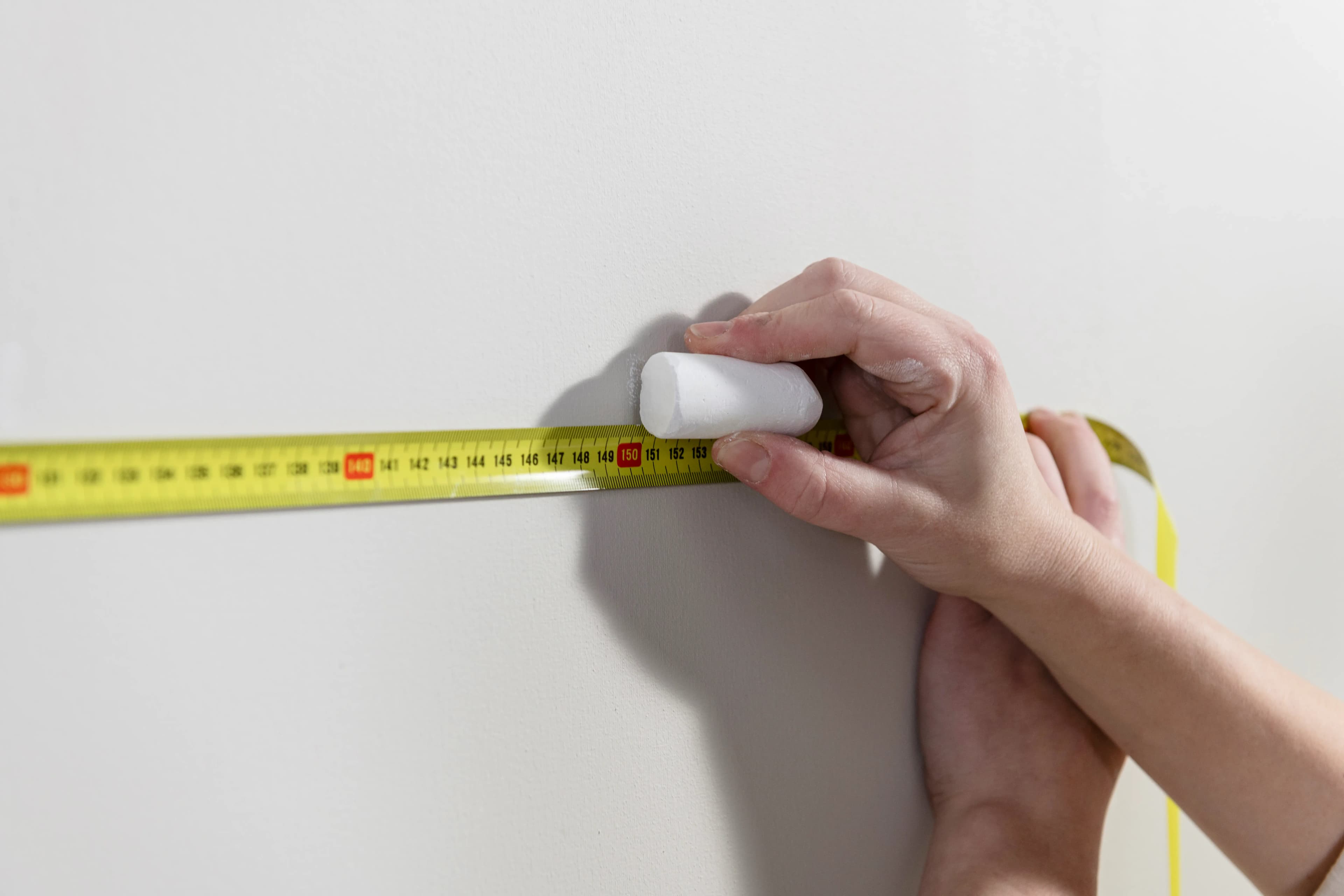 A hand holding chalk next to a wall and tape measure