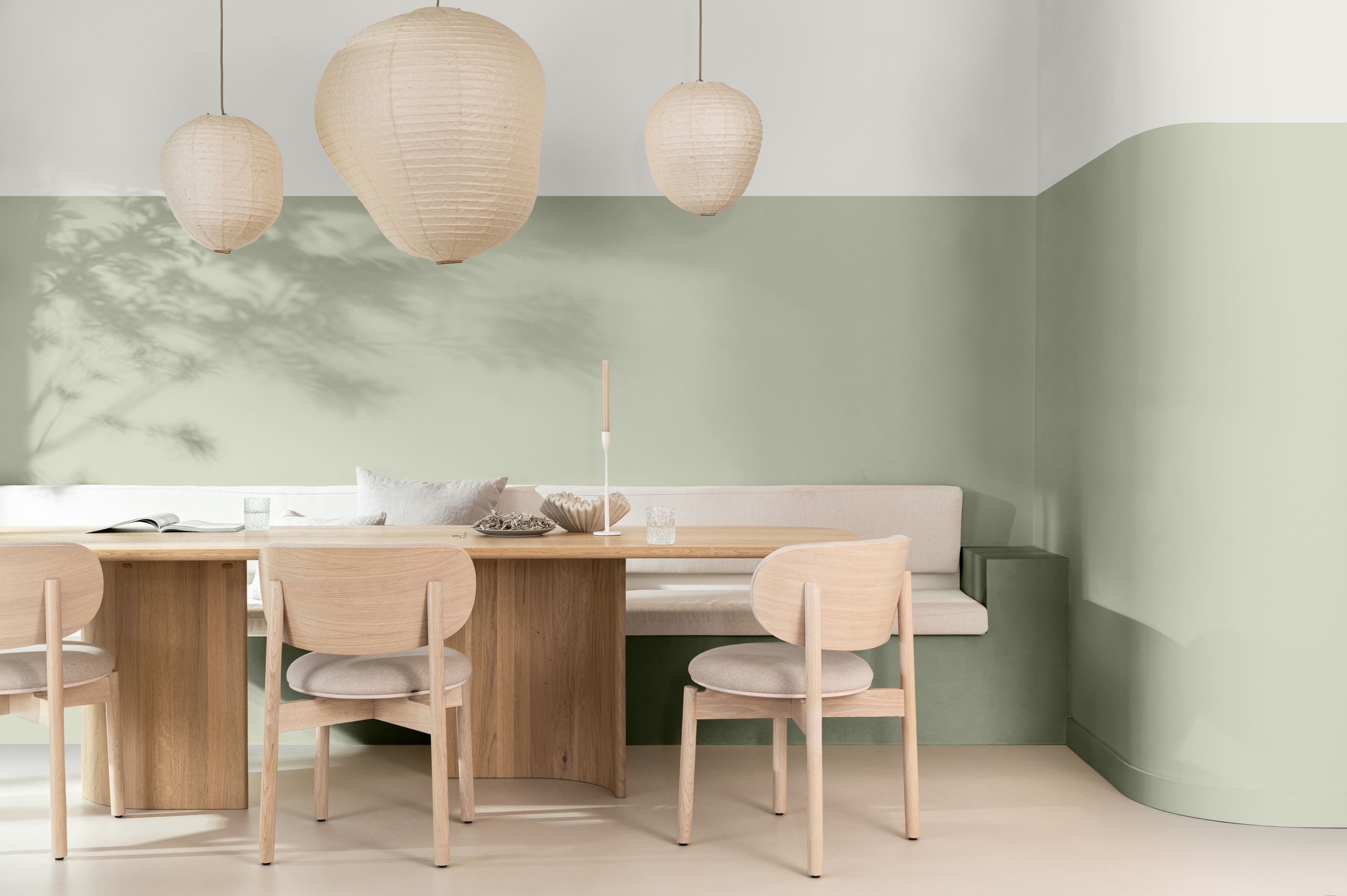 Pale wood dining table and chairs against a sage green wall
